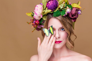 Young woman posing in flower wreath with artificial  greenbutterfly,  isolated on ochet background. One eye closed with a butterfly