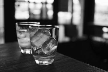 two glass of water and ice cube ont he wooden table in the restaurant in black and white color