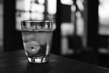 a glass of water with ice cube on the wooden table in the restaurant in black and white color