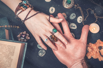 Astrology and esotericism. A fortune teller reads a man's palm. On a black background lie runes, a...