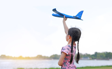 Naklejka premium Portrait of little girl raise up a blue toy airplane flying on air in the nature garden. Back view.