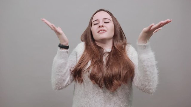 Cheerful charming caucasian woman dancing, smiling, spreads hands wearing fashion blue sweater isolated on gray background in studio. People emotions, lifestyle concept.