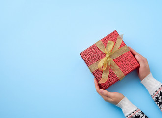 female hand holds a red box tied with a golden ribbon, concept of congratulations and gifts