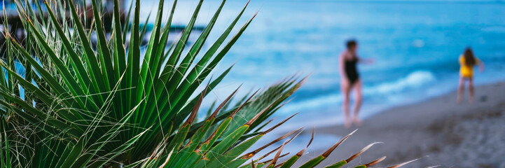 Naklejka premium Bright green tropical leaf view close up with sea and woman with daughter on background. Floral and spa vacation backdrop concept. Web banner for hotel, greeting card idea