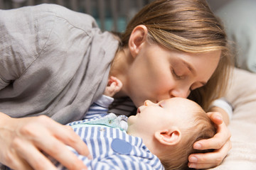 Happy peaceful new mom kissing baby. Portrait of young woman and cute little child in home interior. Motherhood or love concept