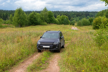 A car stands in a rut on a field overgrown with grass on a summer day