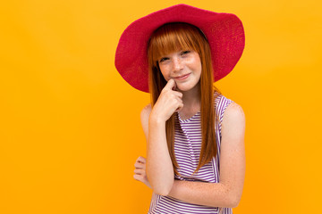 portrait of red-haired attractive pensive tourist girl in a red summer straw hat on a yellow background with copy space