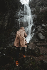 the traveler, wrapped in a jacket, rises on wet dark gray stones to a high powerful waterfall