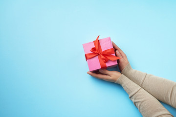 two female hands in a sweater hold closed square pink box with a bow on a blue background