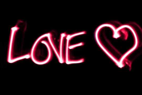Word love white a heart in pink on black background. Light painting.