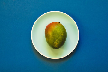 Natural fresh ripe mango fruit in plate on blue background. Flat lay.