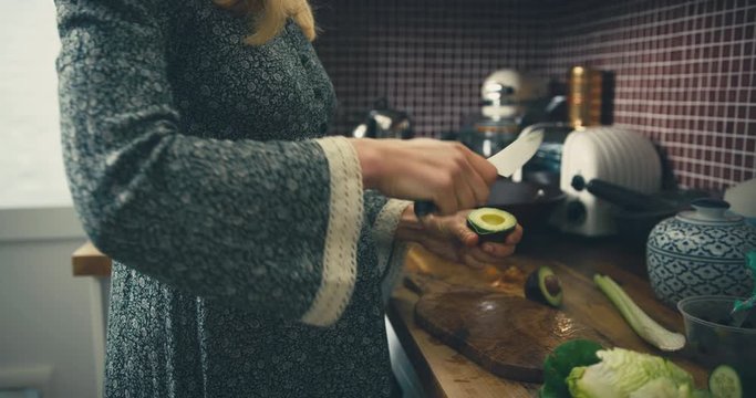 Pregnant woman in kitchen removing skin from avocado