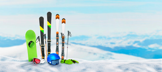 Ski equipment pinned to the snow on top of a mountain. Concept of winter holidays and snow sports. Snowy mountain peaks in the background - obrazy, fototapety, plakaty