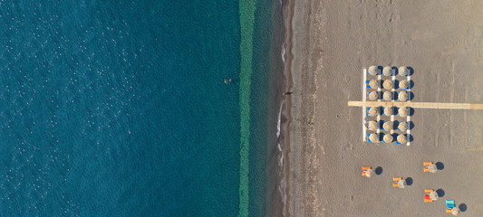 Aerial drone ultra wide top down photo of organised sandy beach in Kamari village, Santorini island, Cyclades, Greece