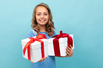 Caucasian child holds many white boxes with gifts and rejoices, portrait isolated on blue background