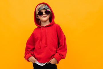 blond boy with a bandana on his head in a red hoodie and glasses posing on an orange background