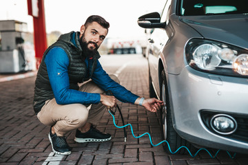 Young handsome adult man standing on gas station and checking tire pressure.