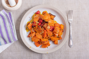 Tasty vegetarian dish - baked sweet potato with onions, carrots and spices in a plate on the table, top view