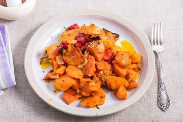 Tasty vegetarian dish - baked sweet potato with onions, carrots and spices in a plate on the table, top view