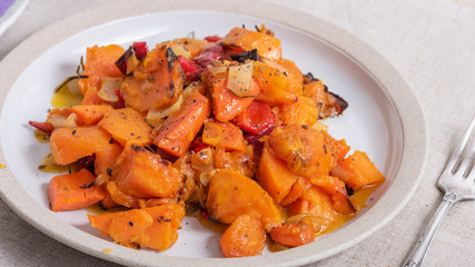 Tasty vegetarian dish - baked sweet potato with onions, carrots and spices in a plate on the table, close-up, rustic style