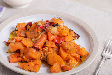 Tasty vegetarian dish - baked sweet potato with onions, carrots and spices in a plate on the table, close-up, rustic style