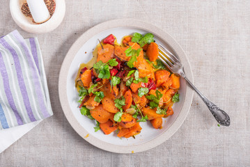 Tasty vegetarian dish - baked sweet potato with onions, carrots and spices in a plate on the table, top view