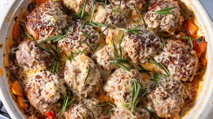 Tasty meatballs in homemade tomato sauce, baked with grated cheese and rosemary leaves in a large enameled pan, close-up, top view