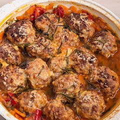 Tasty meatballs in homemade tomato sauce, baked with grated cheese and rosemary leaves in a large enameled pan, close-up, top view