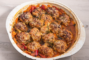 Tasty meatballs in homemade tomato sauce, baked with grated cheese and rosemary leaves in a large enameled pan, top view