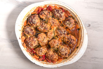 Tasty meatballs in homemade tomato sauce, baked with grated cheese and rosemary leaves in a large enameled pan, top view