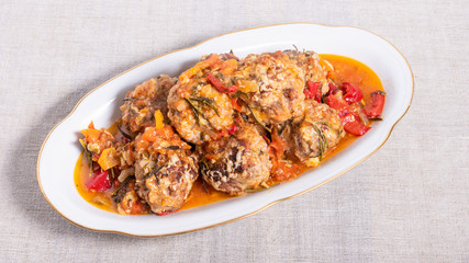 Delicious meatballs in homemade tomato sauce, baked with grated cheese and rosemary leaves on an oval dish