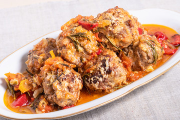 Delicious meatballs in homemade tomato sauce, baked with grated cheese and rosemary leaves on an oval dish