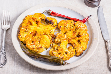 Baked cauliflower steaks sprinkled with spices on a plate with chili pepper pods, top view, close-up
