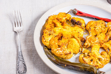 Baked cauliflower steaks sprinkled with spices on a plate with chili pepper pods, top view, close-up
