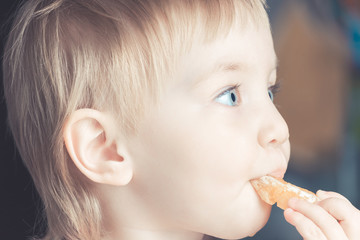 Beautiful child with big blue eyes eating orange slice