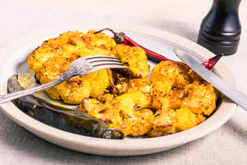 Tasty baked cauliflower steaks sprinkled with spices on a plate with chili pepper pods closeup - vegetarian cuisine