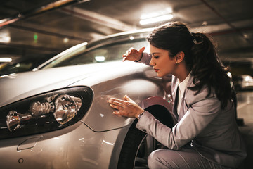 Frustrated and terrified young businesswoman looking at her scratched car.