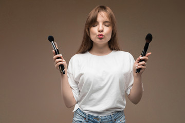 nice girl with closed eyes holds makeup brushes in two hands on a dark brown background
