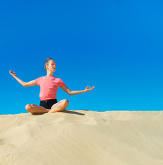 ein junges Mädchen macht im Sommer Yoga auf einer Düne im gelben Sand vor blauem Himmel