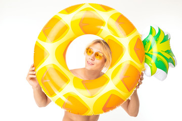 handsome blond man peeps out a swimming circle in the form of pineapple on a white background