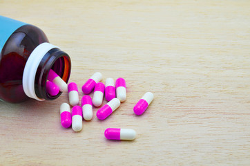 Medication spilling from an open bottle on a wooden background.