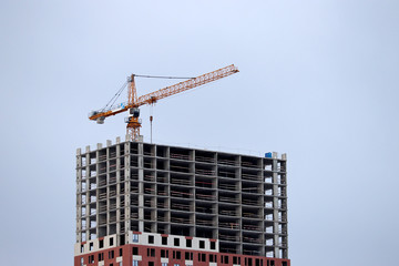 Construction crane and high-rise building on background of blue sky. Housing construction, apartment block