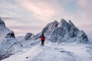 Traveler standing with hiking poles on top of Segla mountain in winter at Senja Island