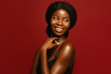 Beauty. African American beautiful woman portrait. Brunette curly haired young model with dark skin and perfect smile against red background - obrazy, fototapety, plakaty