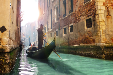 Gondolier rowing gondola in canal with green water