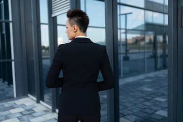 short-haired business lady in a jacket stands with her back and walks to the front door of a modern office building