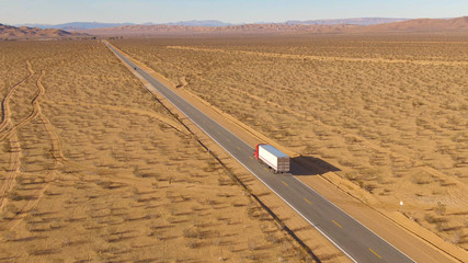 DRONE: Freight truck driving along the highway leading across Mojave desert.