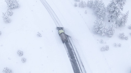 Obraz na płótnie Canvas DRONE: Truck plowing and salting a road crossing the scenic wintry countryside.