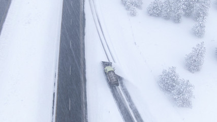 AERIAL: Snow ploughing truck clears and salts a highway lane during a snowstorm.