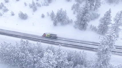 DRONE: Snow ploughing truck cleans the country road leading through the forest.